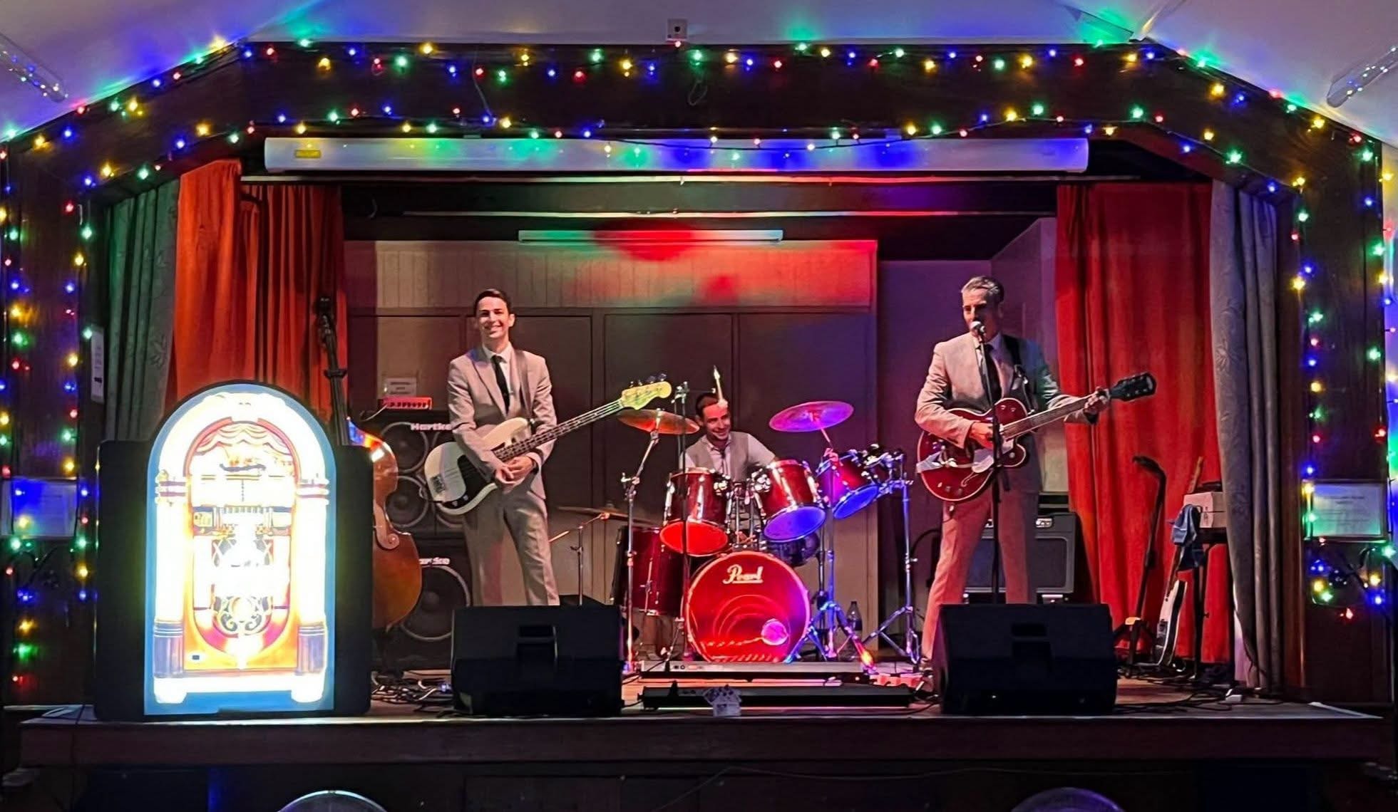 Full band on stage with jukebox prop and fairy lights